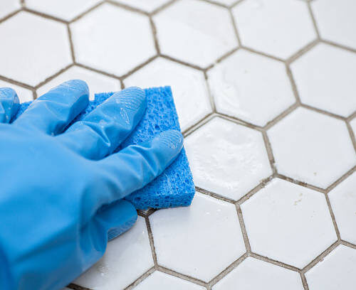 a person wearing blue gloves holds a sponge cleaning a white tile floor a person wearing blue gloves holds a sponge cleaning a white tile floor
